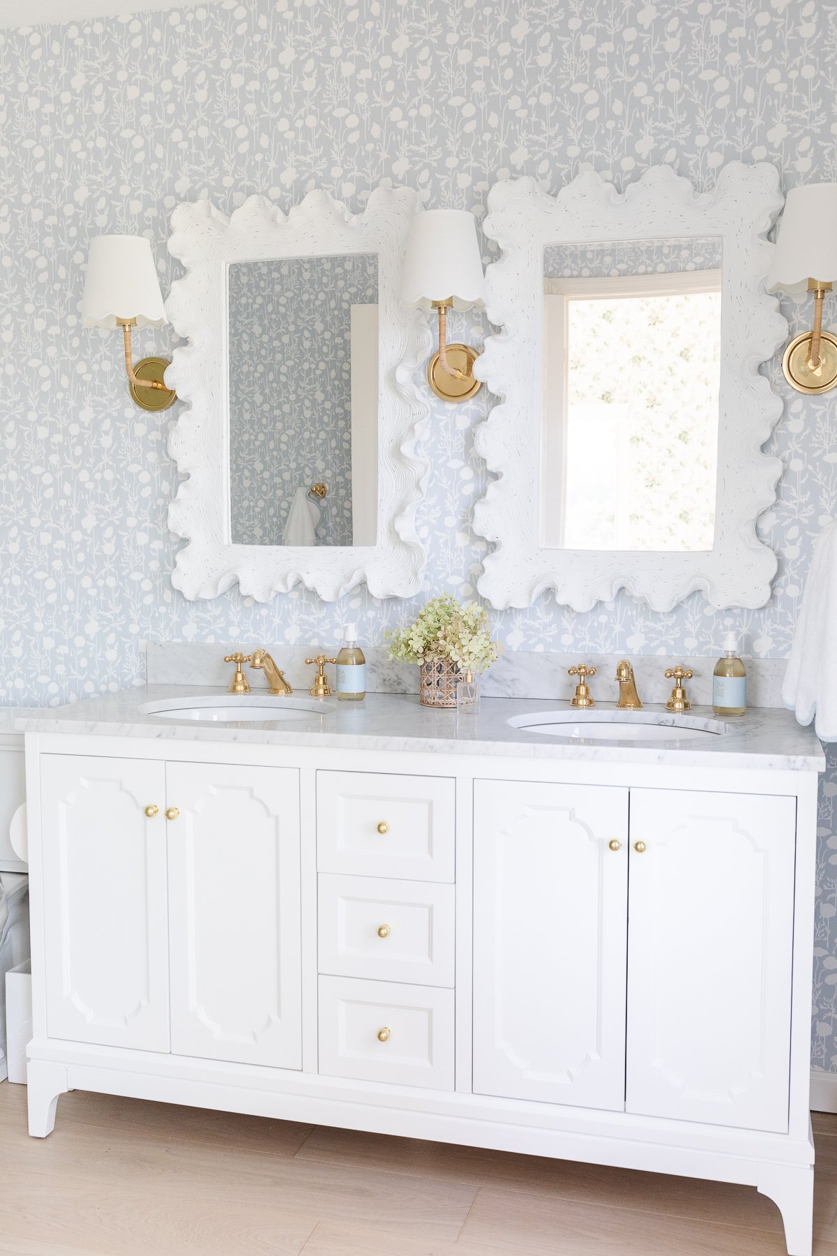 A soft blue and white wallpapered bathroom with a double white bathroom vanity.