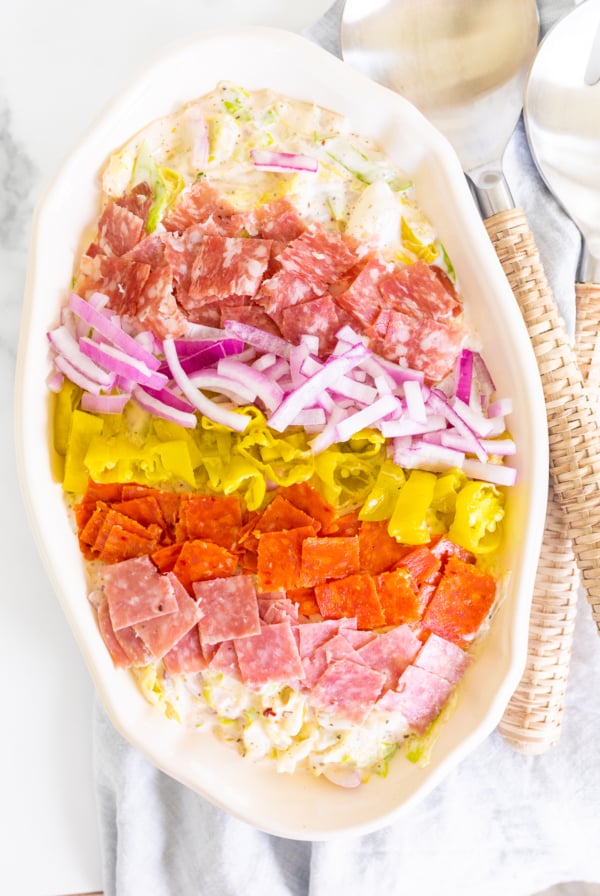 A grinder salad recipe in a white oval bowl, with rattan serving utensils to the side.