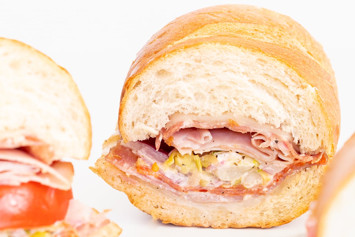An Italian grinder sandwich, sliced in half on a white plate.