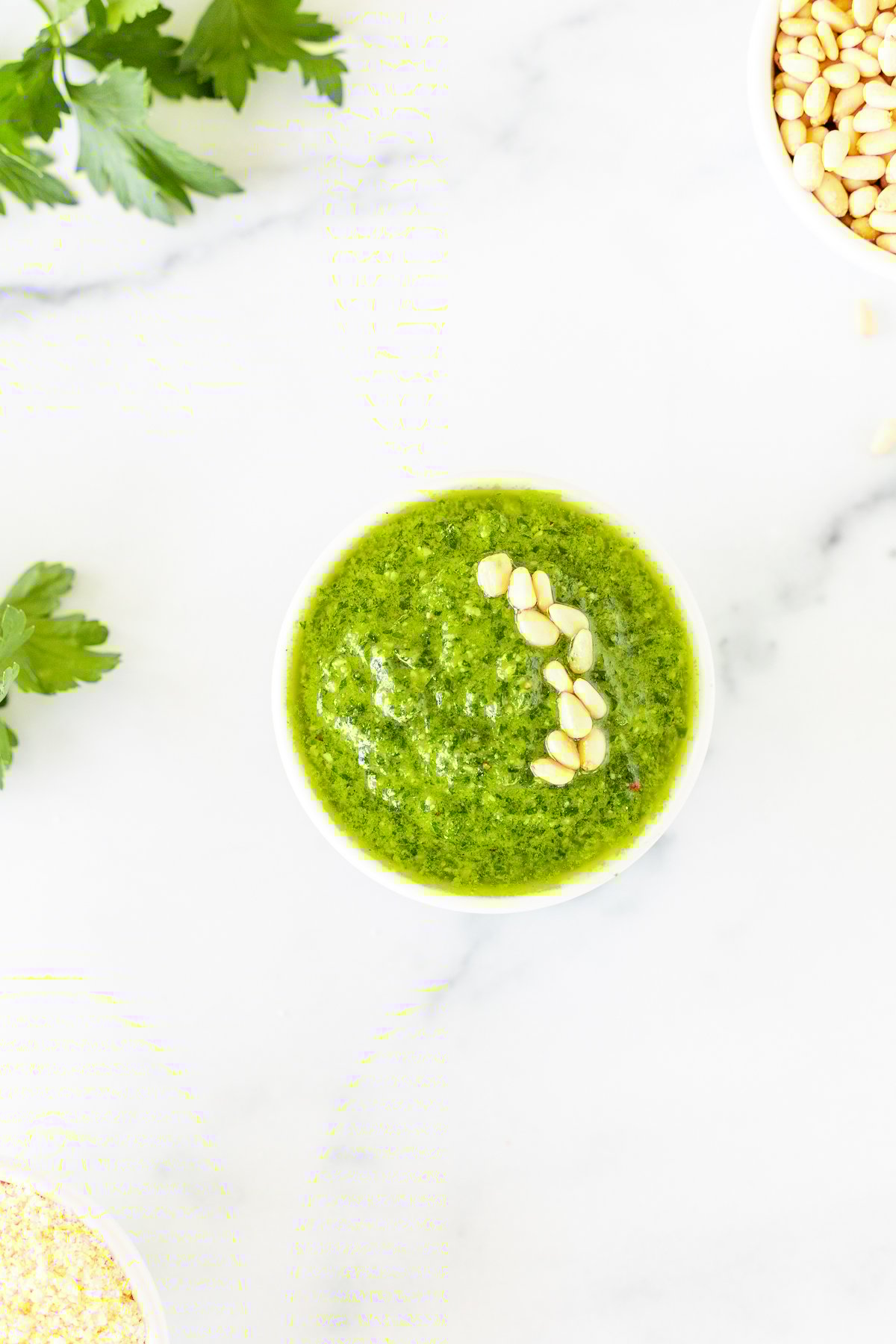 A white bowl of fresh pesto parsley on a white countertop.