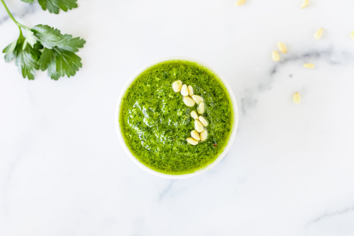 A white bowl of fresh pesto parsley on a white countertop.