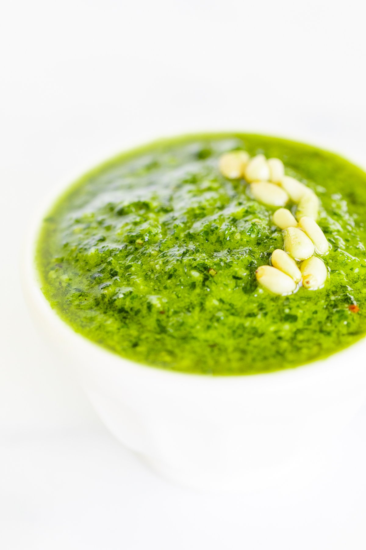 A white bowl of fresh pesto parsley on a white countertop.