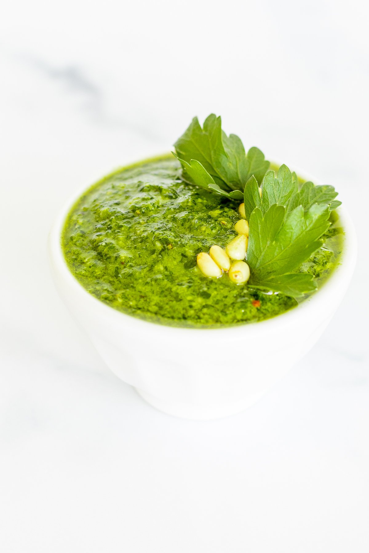 A white bowl of fresh pesto parsley on a white countertop.