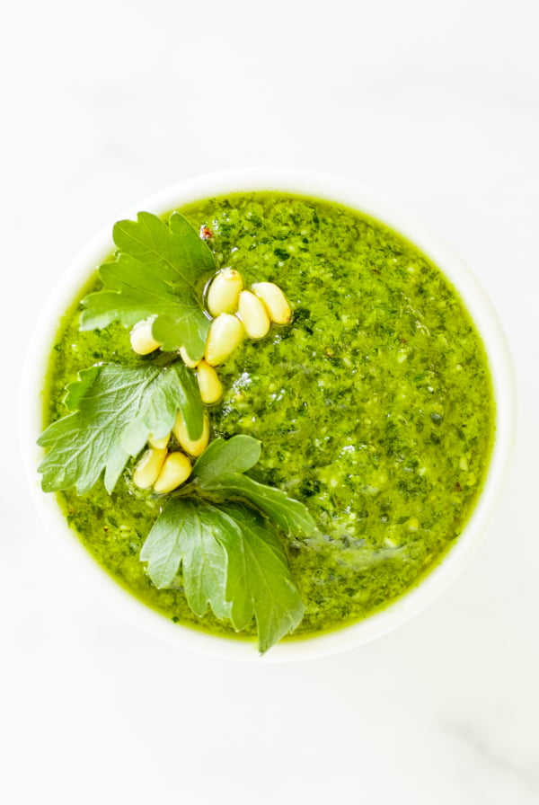 A white bowl of fresh pesto parsley on a white countertop.