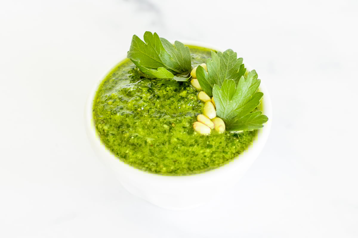 A white bowl of fresh pesto parsley on a white countertop.