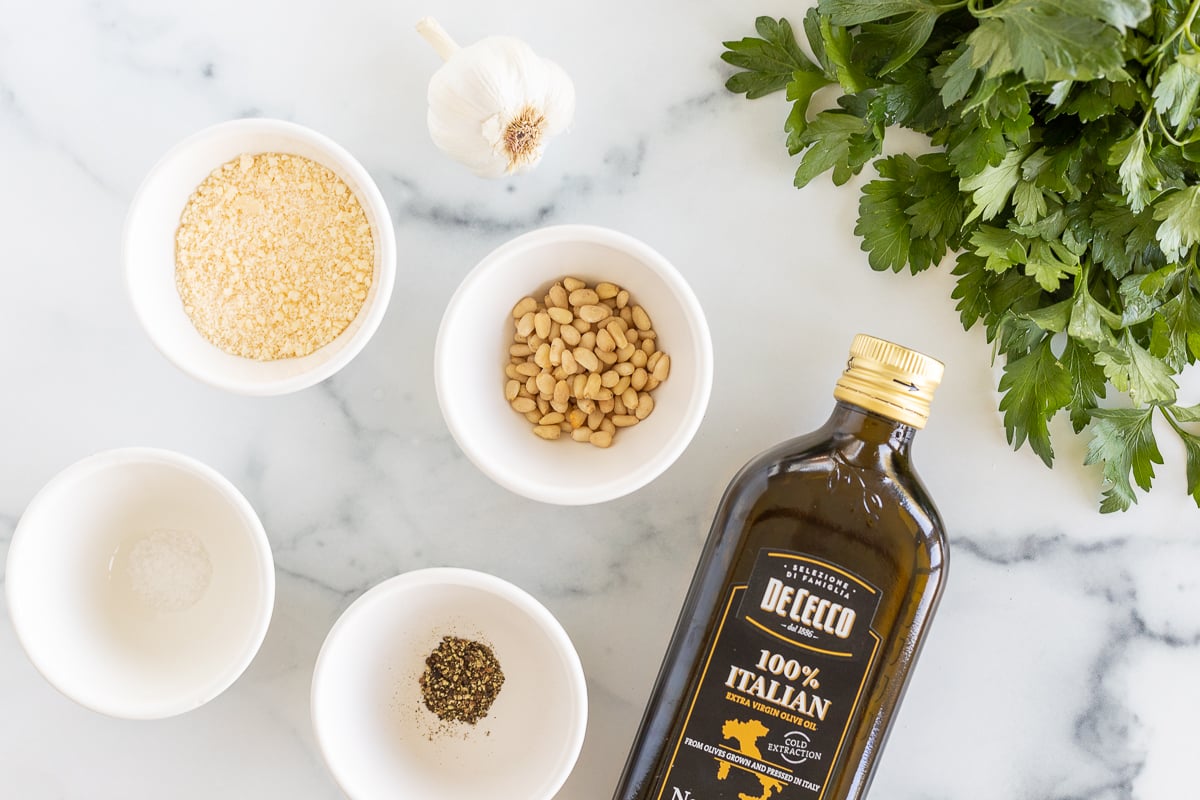 Ingredients for a pesto with parsley on a white marble countertop.