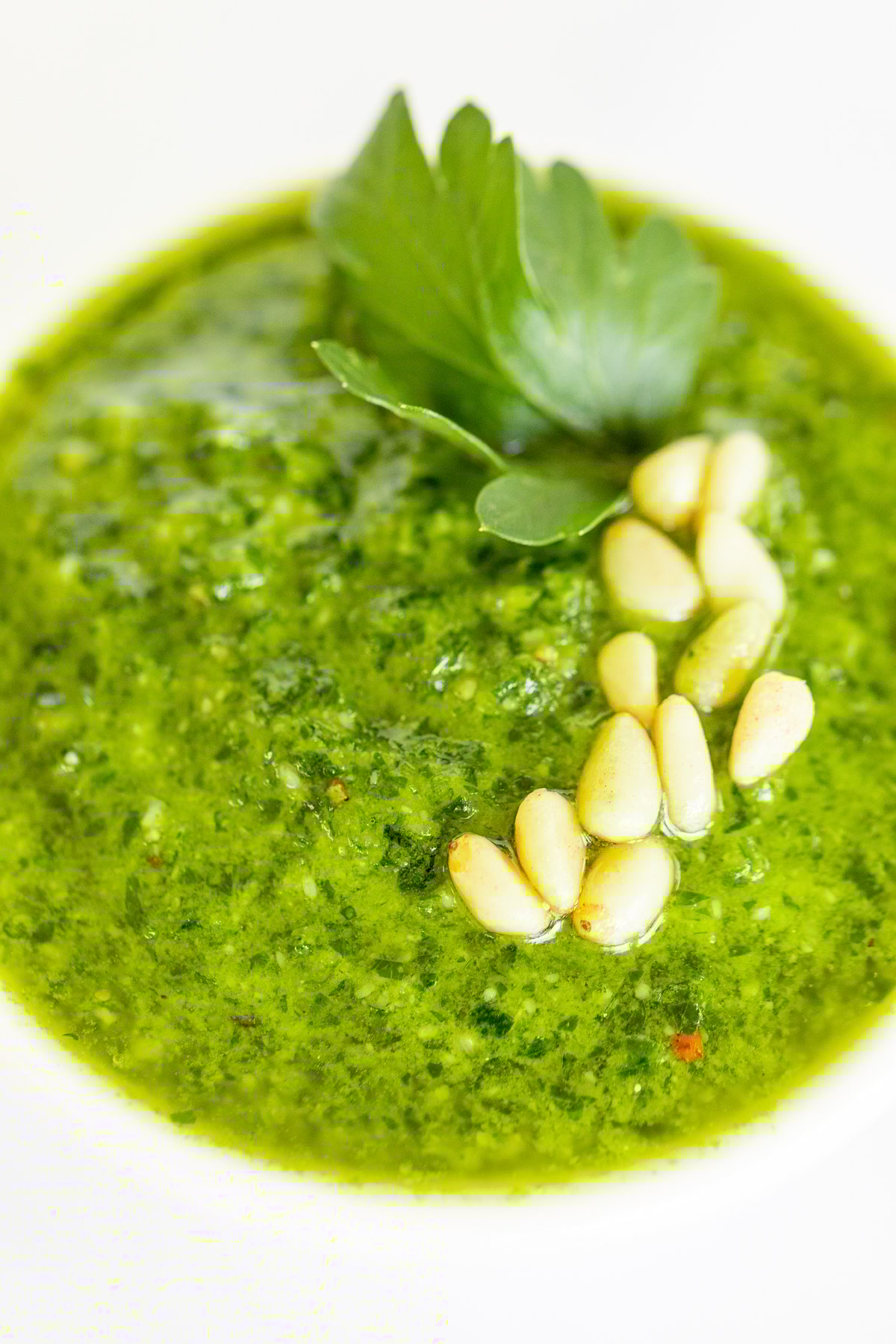 A white bowl of fresh pesto parsley on a white countertop. 