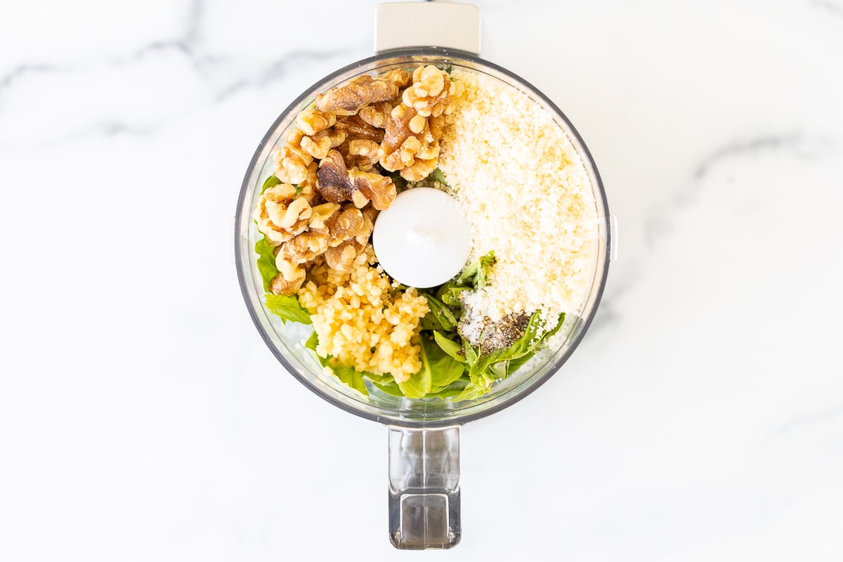 Ingredients for walnut pesto in a clear food processor base.