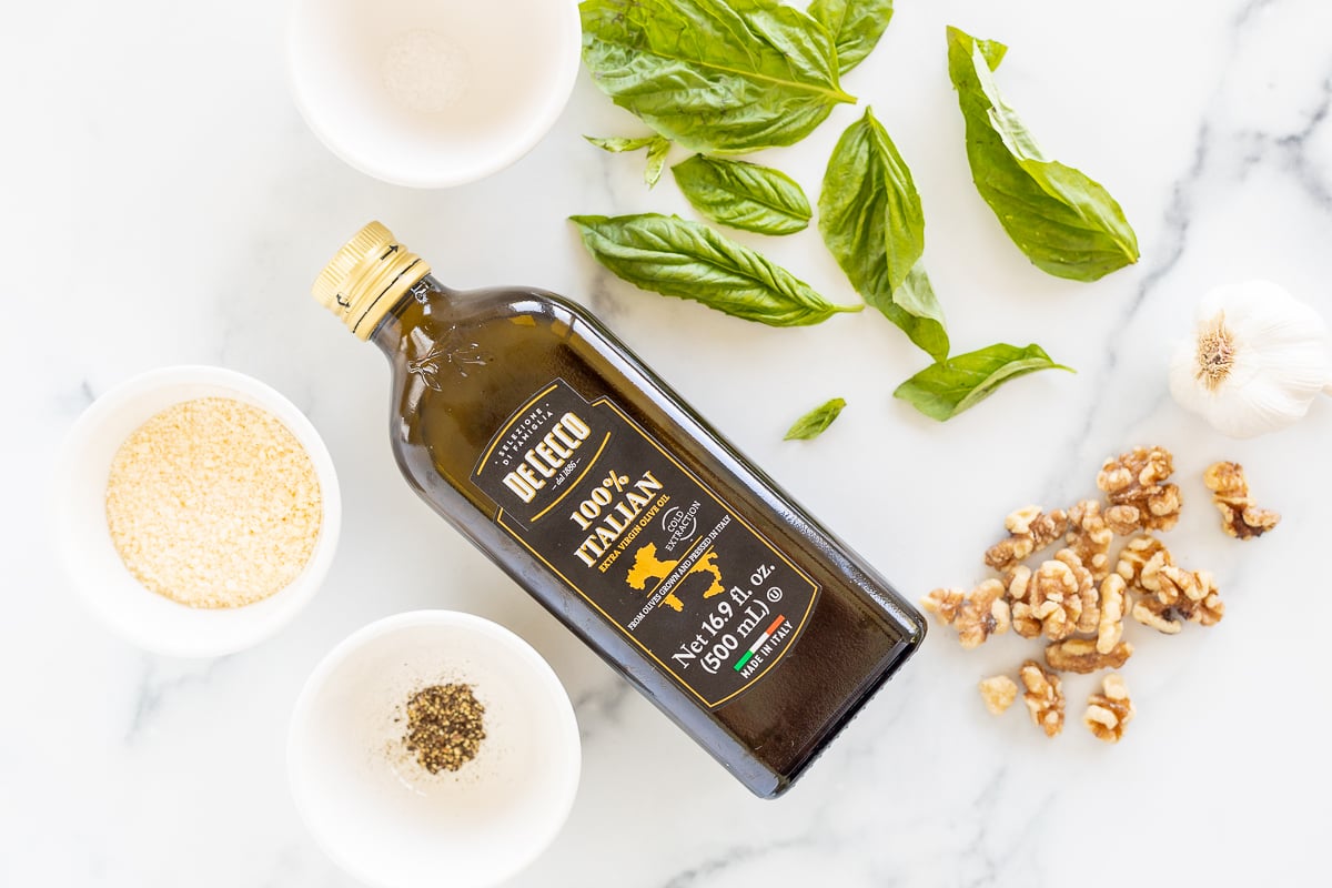 Ingredients for a walnut pesto recipe on a white countertop.