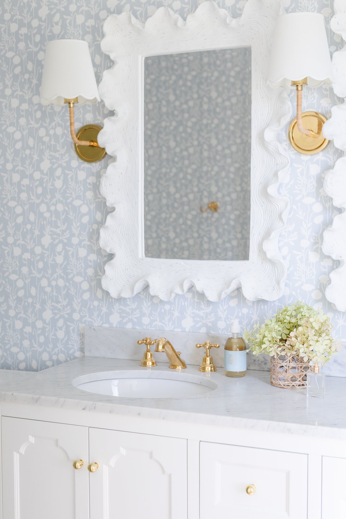 A soft blue and white wallpapered bathroom with a double white bathroom vanity.