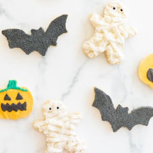 A variety of bat, jack o lantern and mummy Halloween sugar cookies laid out on a marble countertop.