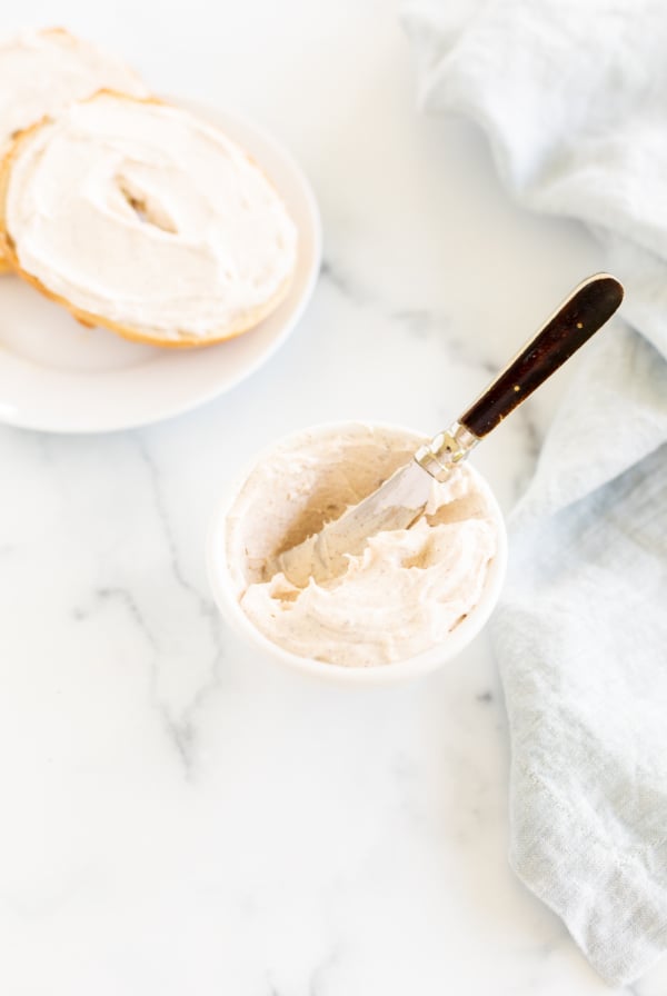 A bowl of cream cheese with a spoon next to a baguette.