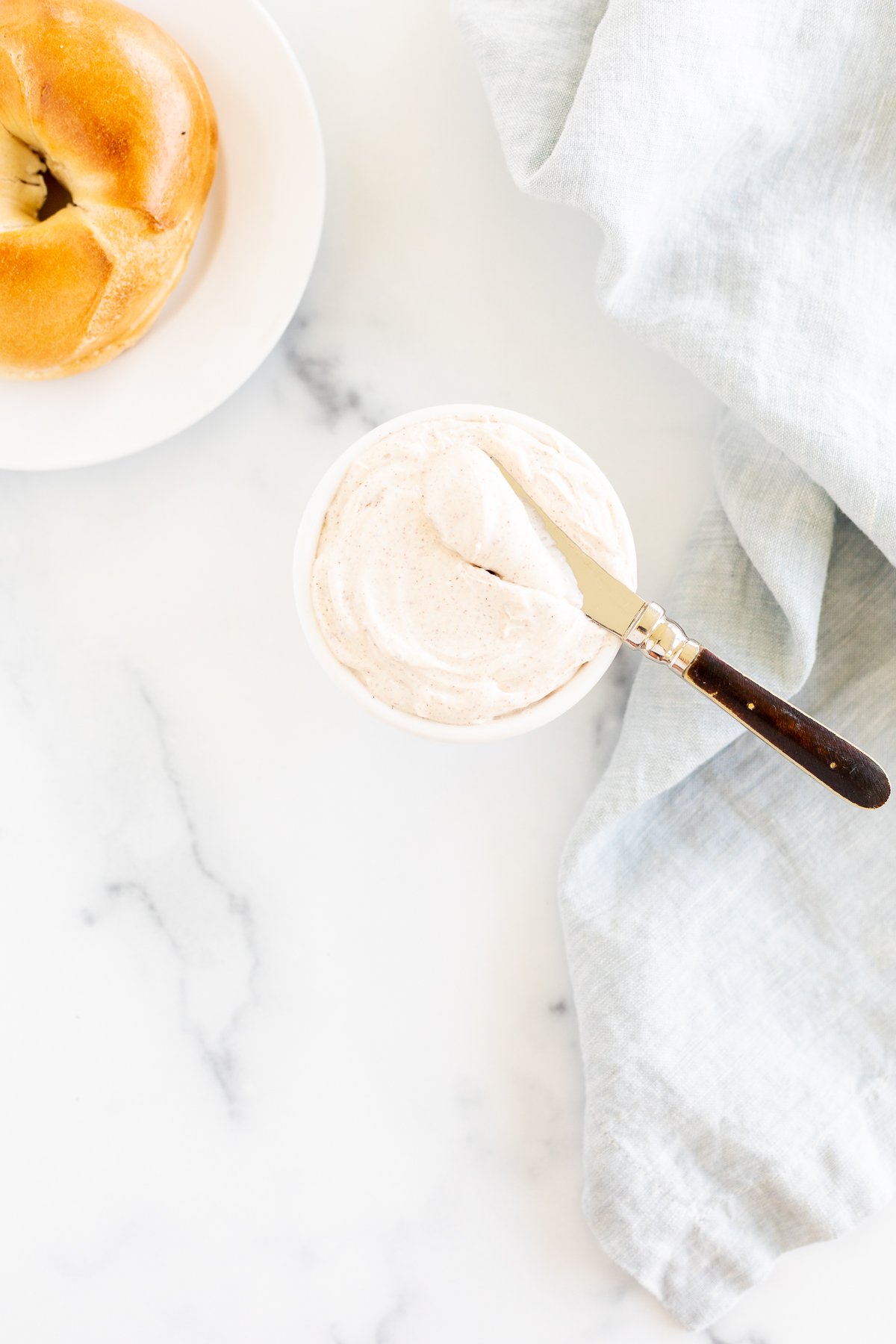 A bowl of cinnamon cream cheese and a bagel on a white table.