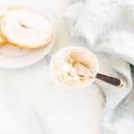 A bowl of cinnamon cream cheese and a bagel on a white table.