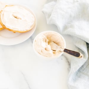 A bowl of cinnamon cream cheese and a bagel on a white table.