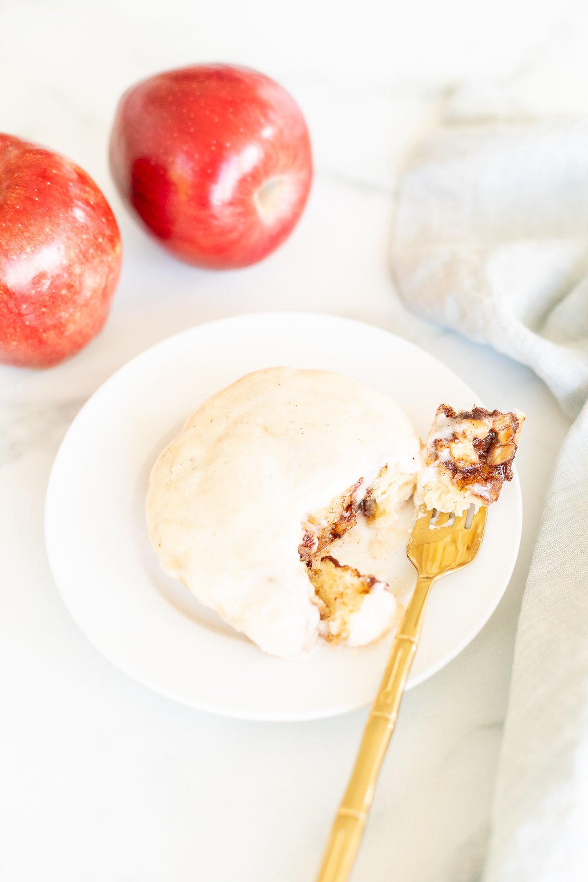 A white plate with a gold fork next to a plate of apple cinnamon rolls.