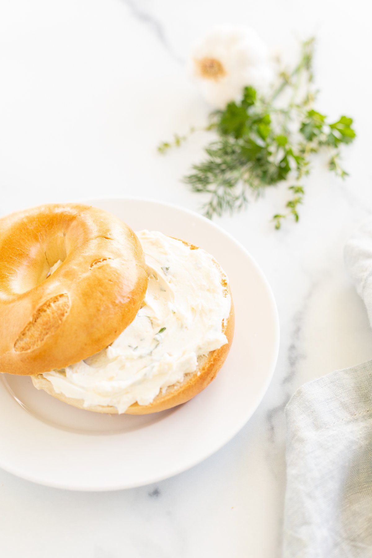 A bagel topped with garlic and herb cream cheese on a white plate.