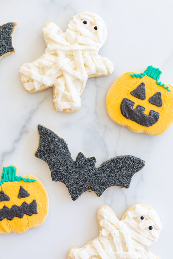 A variety of bat, jack o lantern and mummy Halloween sugar cookies laid out on a marble countertop.