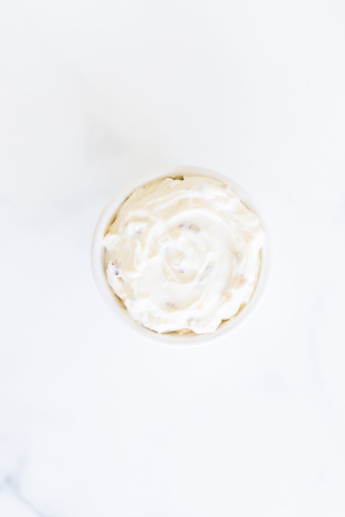 A white bowl of honey walnut cream cheese on a white surface.