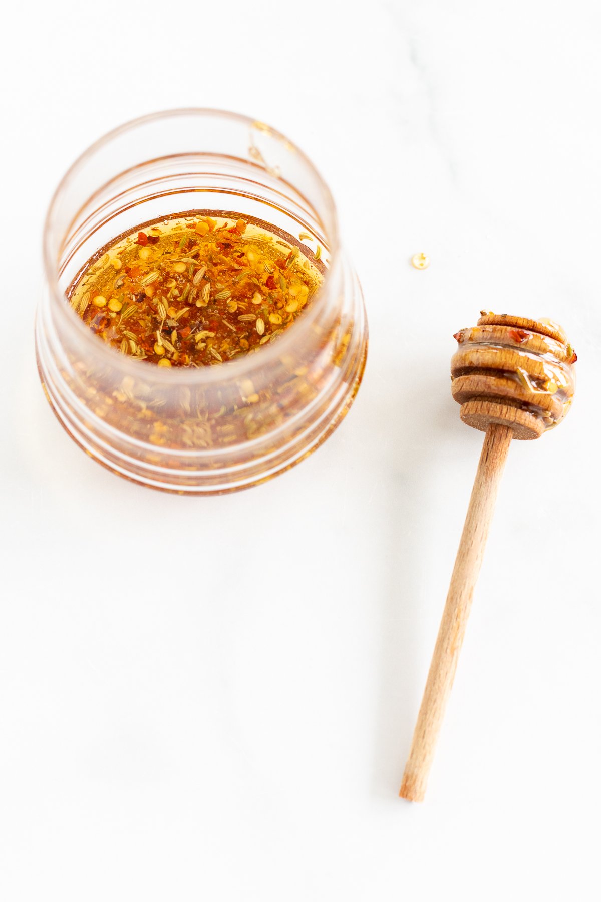 A wooden spoon with honey on it next to a glass jar of hot honey.