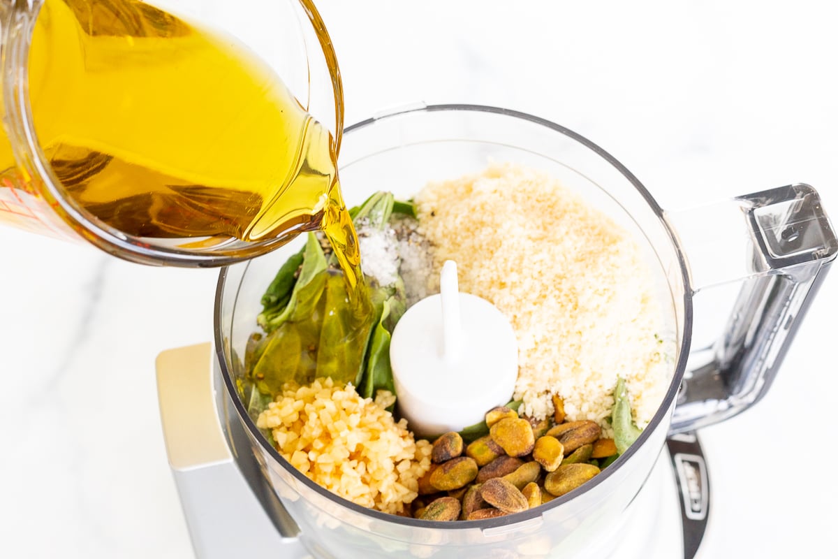 Pistachio pesto being poured into a food processor, incorporating olive oil.