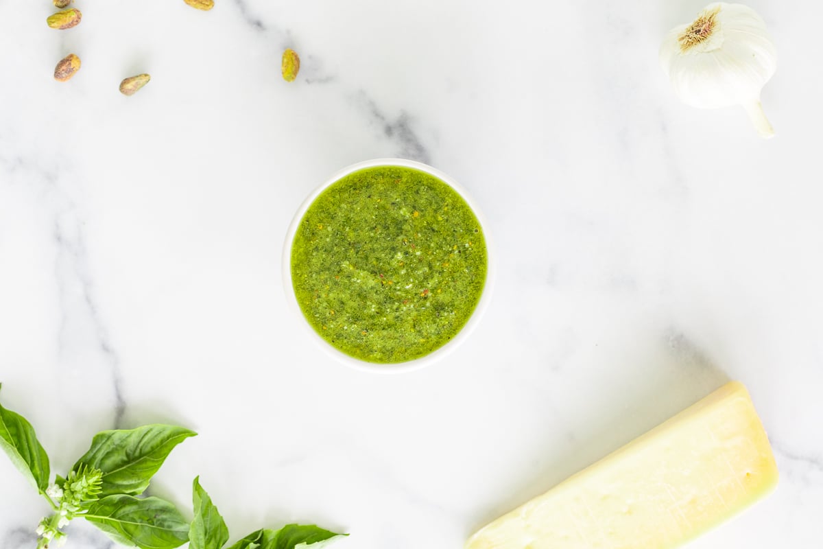 A bowl of pistachio pesto sauce on a marble countertop.