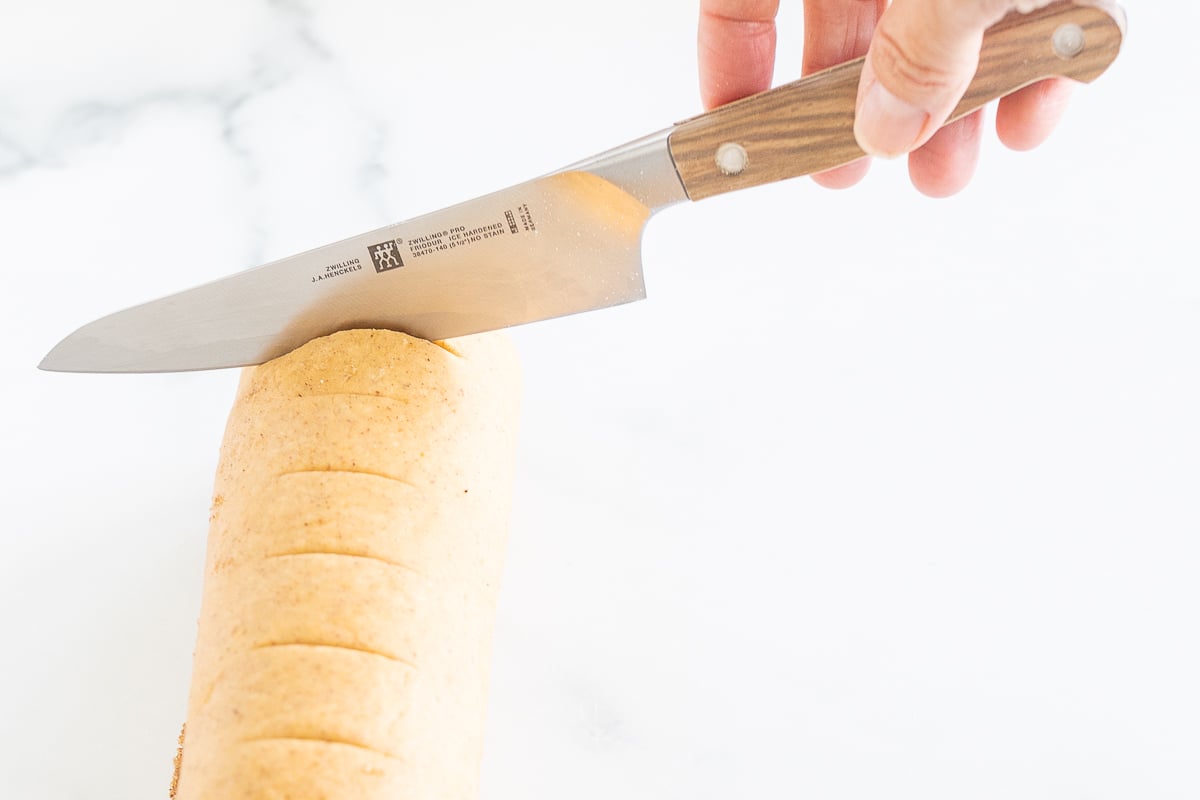 A person cutting a loaf of bread with a knife to make Pumpkin Cinnamon Rolls.