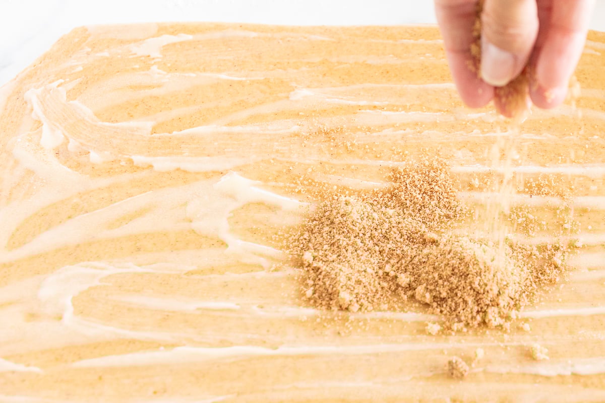 A person is sprinkling sugar on a Pumpkin Cinnamon Rolls.