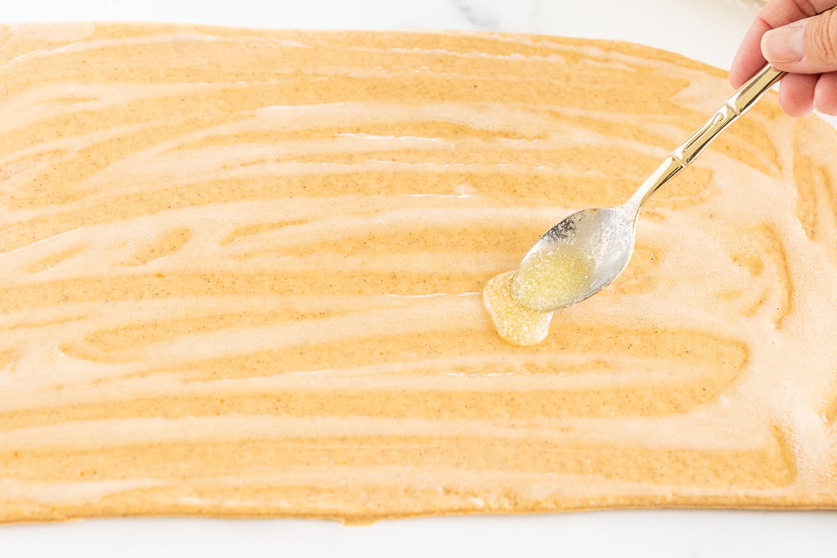 A person is using a spoon to drizzle icing on a Pumpkin Cinnamon Rolls.