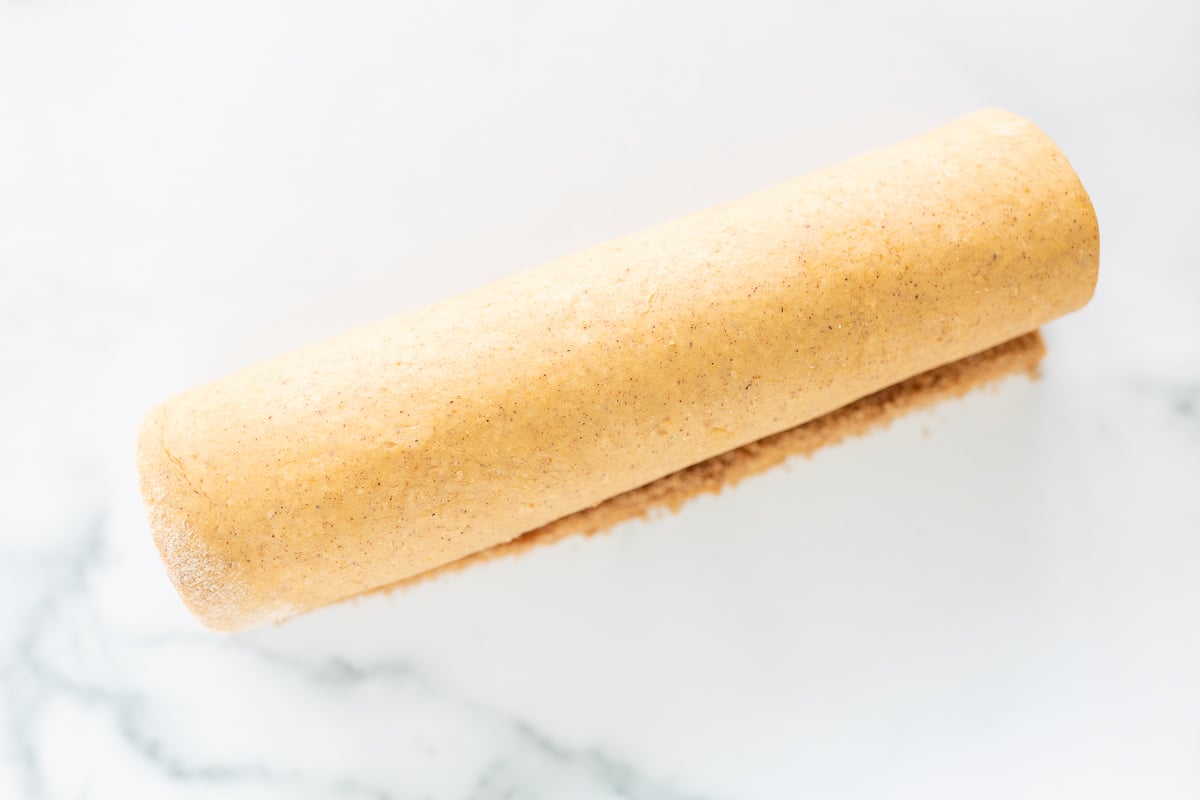 A roll of pumpkin cinnamon dough sitting on top of a marble surface.
