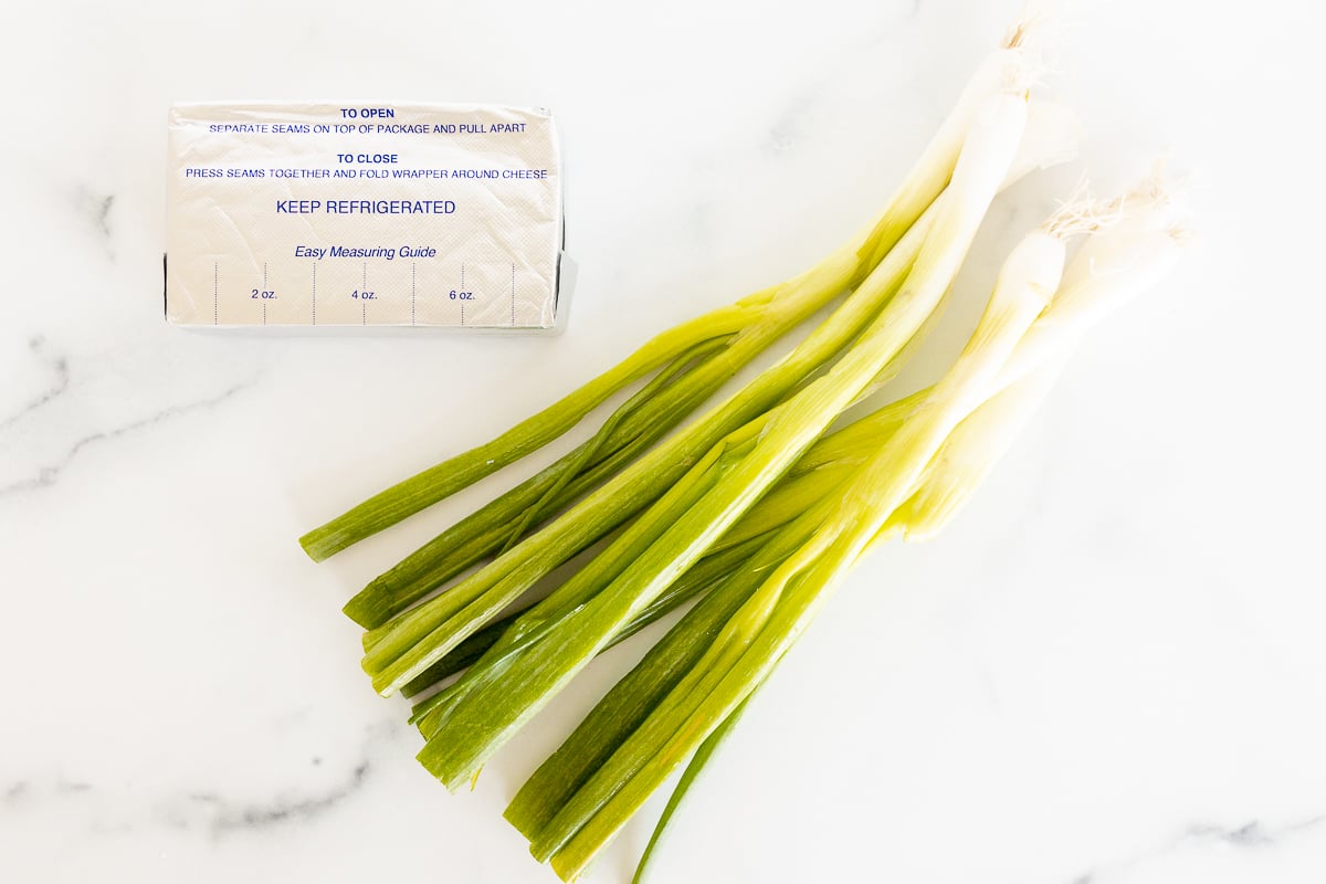 A bunch of green onions on a marble countertop, with a bundle of scallions to the side.