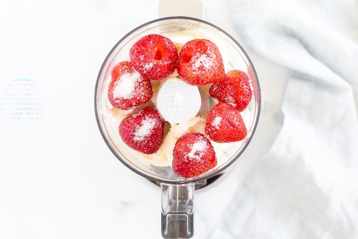 A food processor filled with strawberries and sugar.