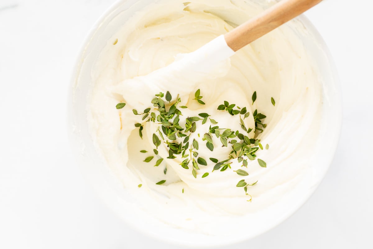 A bowl of whipped ricotta with herbs and a wooden spoon.