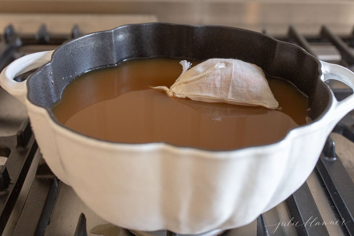 A tea bag filled with mulling spices in a pot of cider