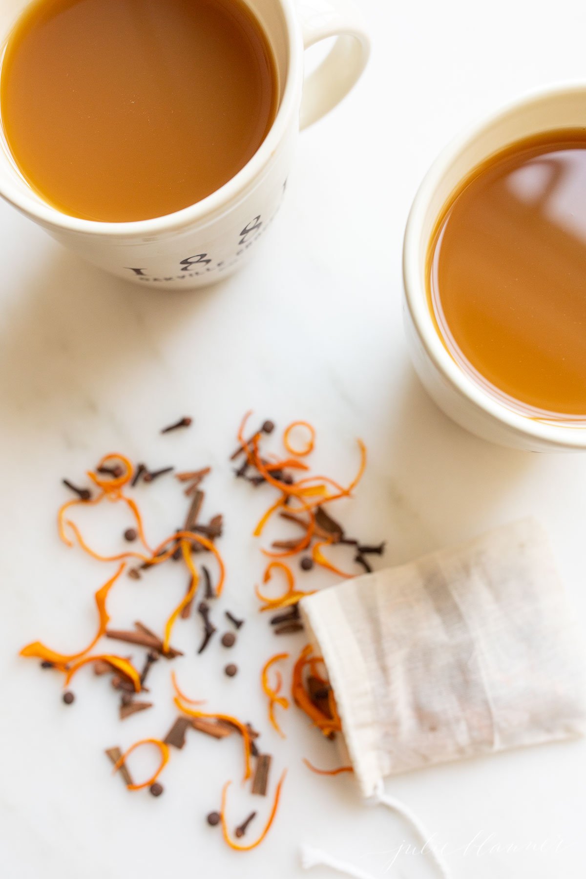 Two cups of cider with a bag of mulling spices spilled in front.