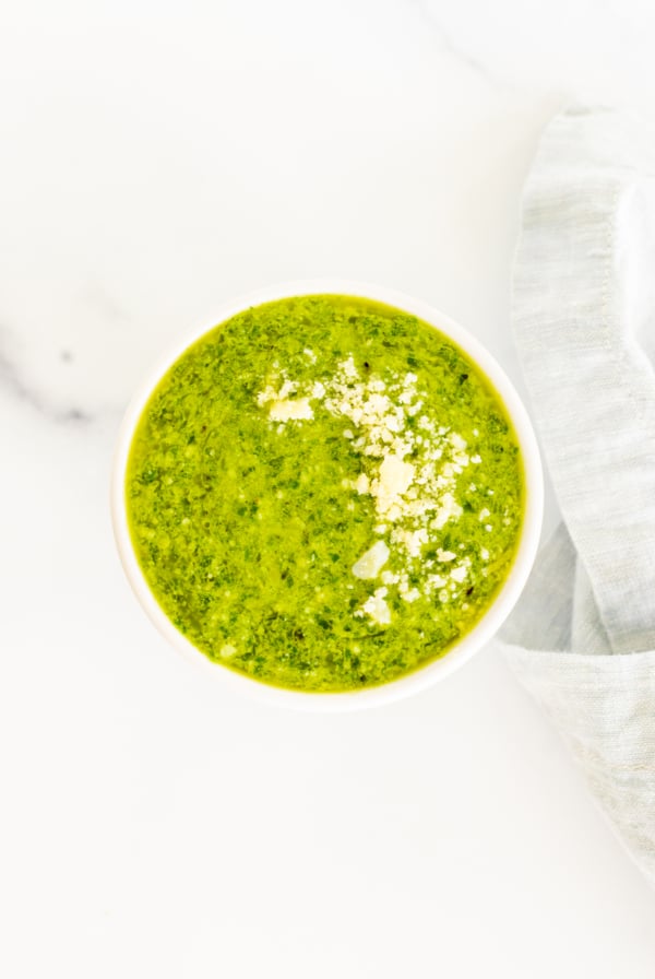 A bowl of green Nut Free Pesto soup on a white table.