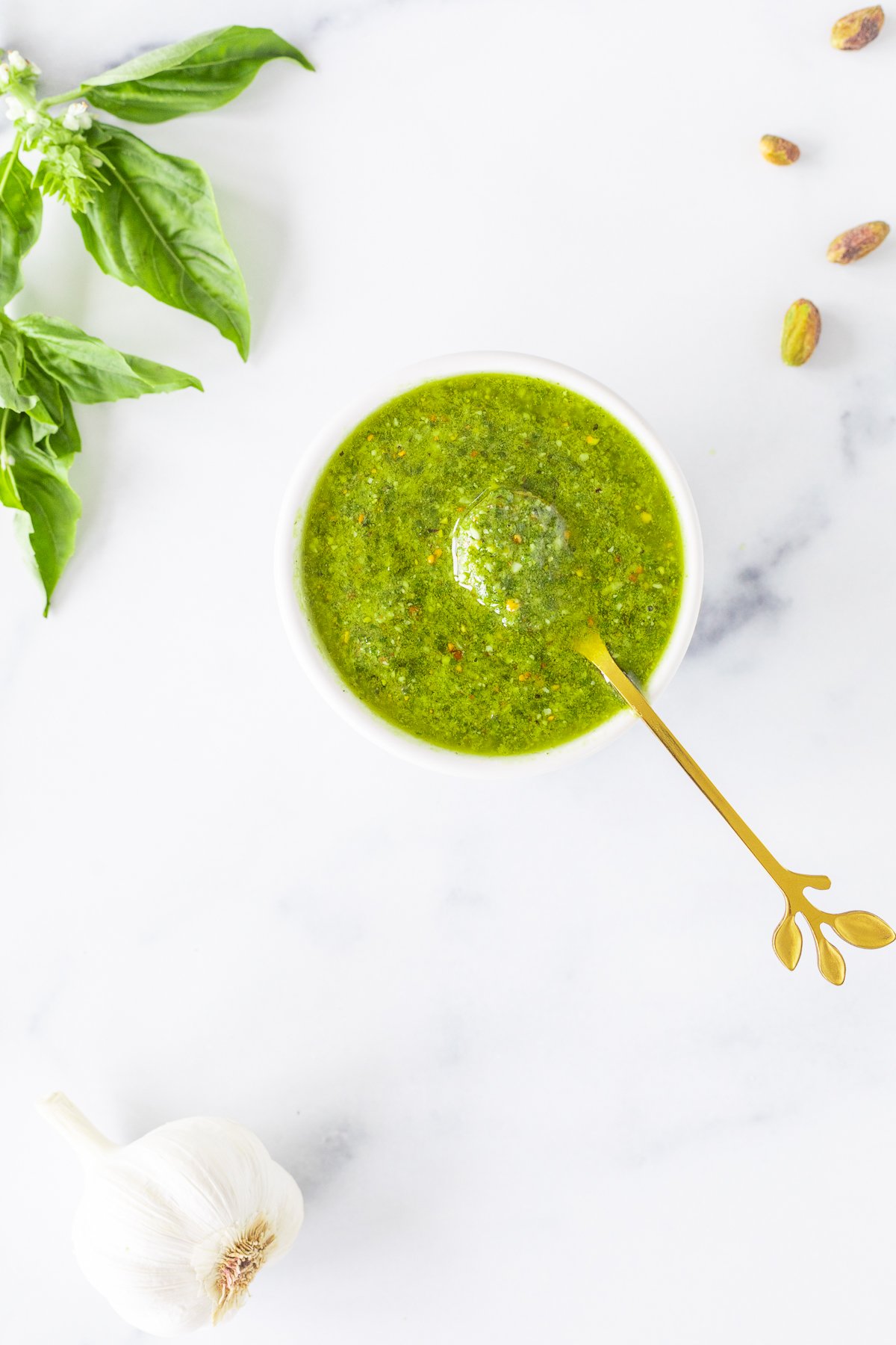 Pistachio Pesto sauce in a white bowl with garlic and basil.