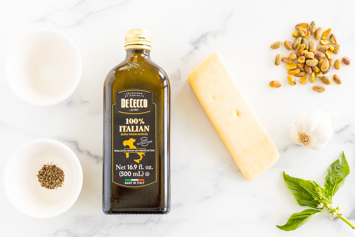 A bottle of Pistachio Pesto and other ingredients on a marble table.