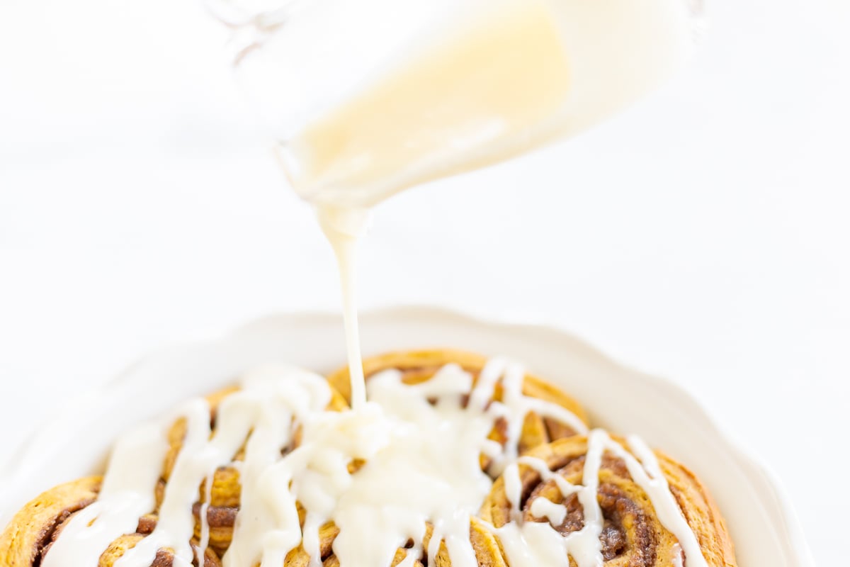 Pumpkin cinnamon rolls with icing being poured onto a plate.