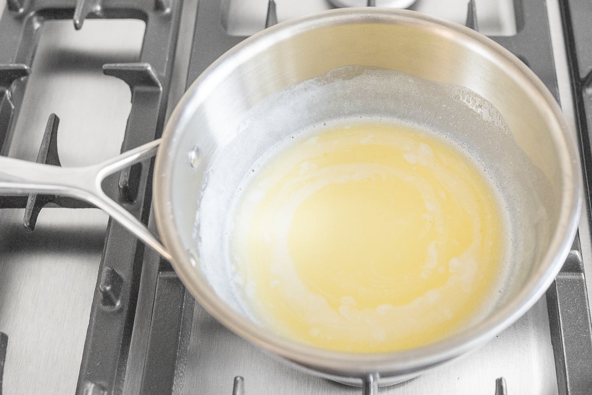 A pan with liquid in it on a stove top, simmering pumpkin cinnamon rolls.