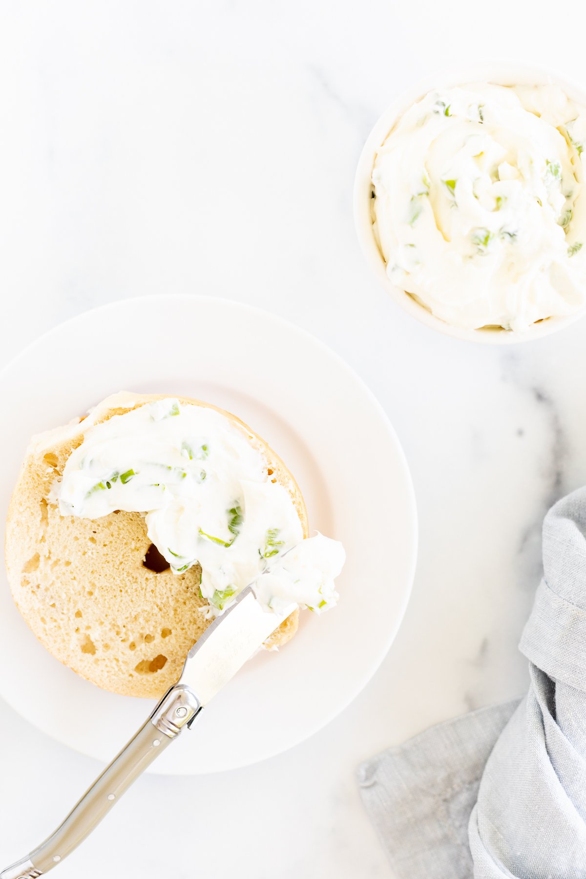 A white plate with a bagel and scallion cream cheese on it.