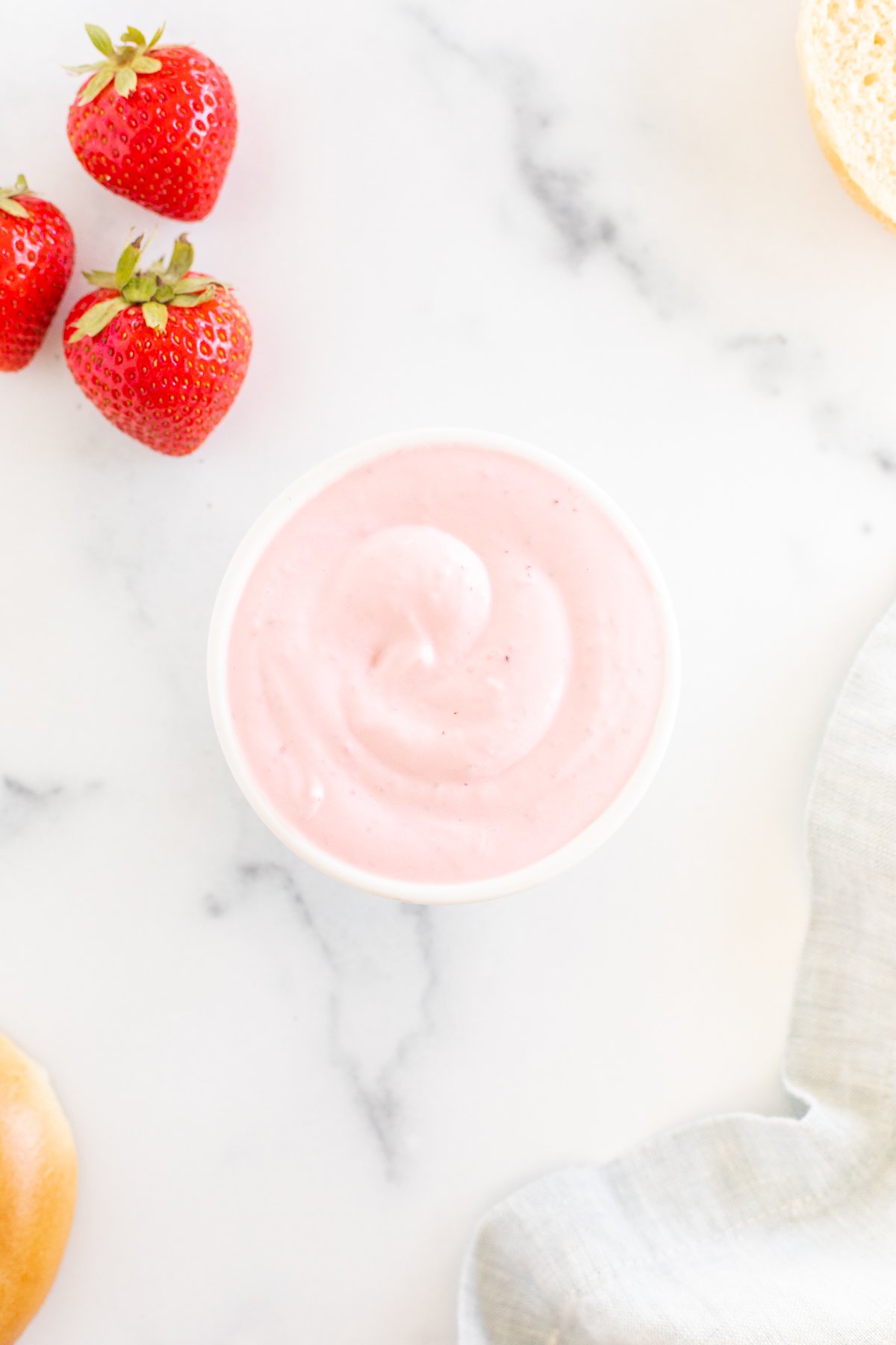 A bowl of strawberry cream cheese on a marble table.