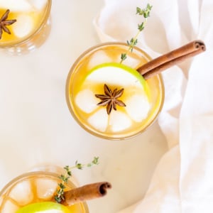 A glass of apple cider with cinnamon sticks and ice, perfect for Thanksgiving drinks.