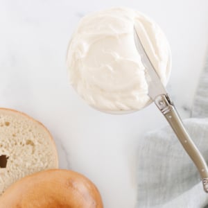 A bagel with whipped cream cheese and a knife next to it.