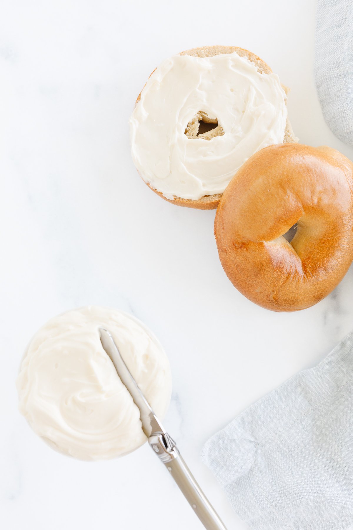 A whipped cream cheese bagel with a knife next to it.