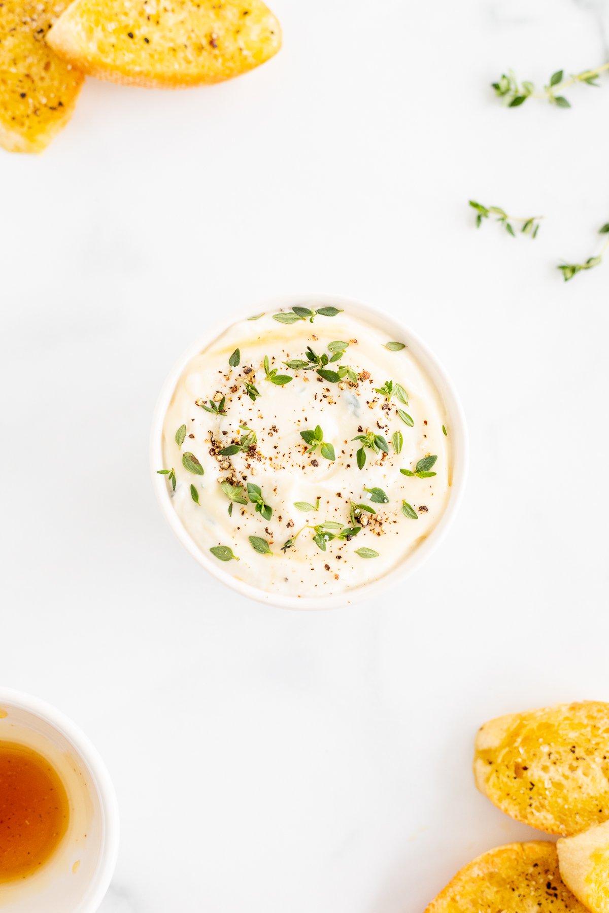 A bowl of whipped ricotta dip with bread and herbs.