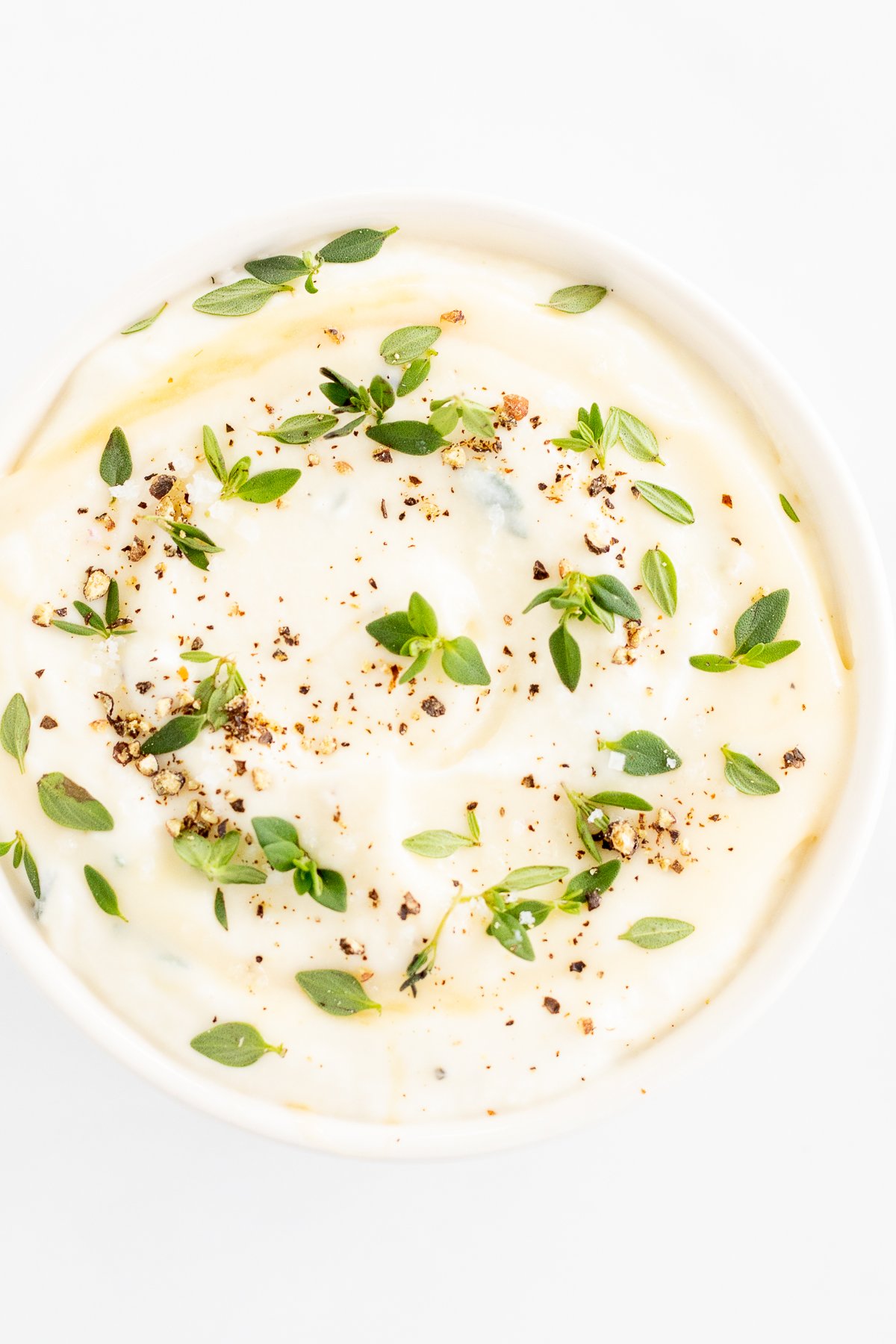 A white bowl of whipped ricotta with a sprig of thyme.