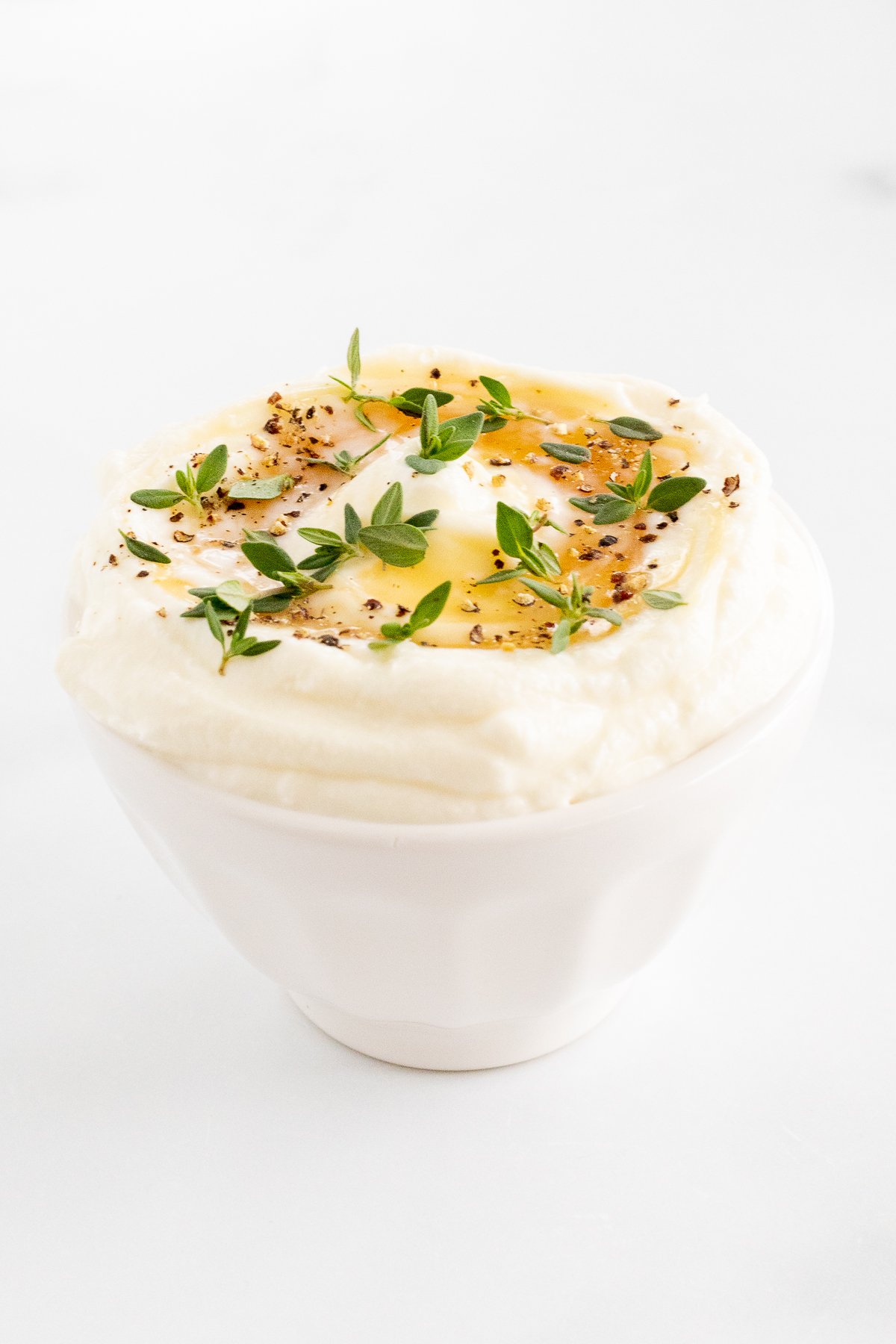 A white bowl of whipped ricotta with a sprig of thyme.