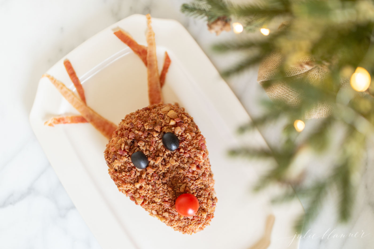 A reindeer Christmas cheese ball on a plate next to a christmas tree.