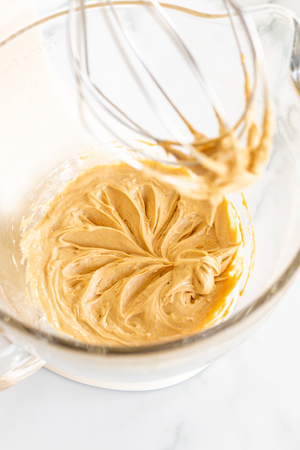 A glass bowl with a whisk in it, ready for whipping together the indulgent ingredients for cookie butter cinnamon rolls.